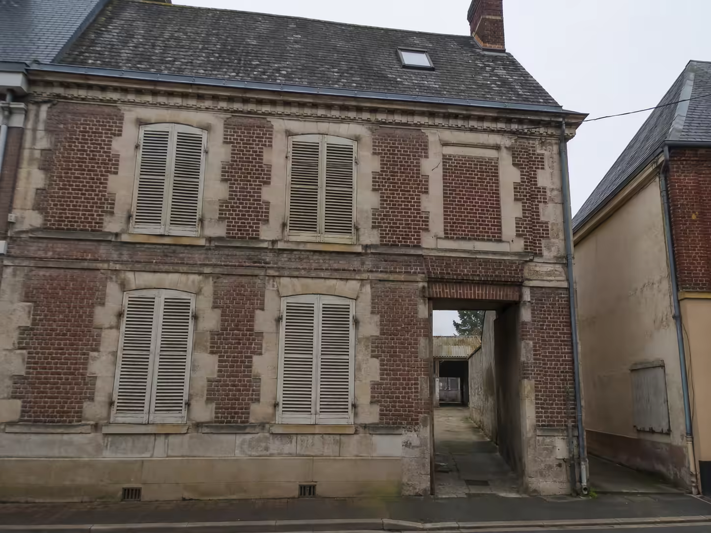 Maison de centre-ville à Cambrai avec façade en brique et pierre, toiture haute en ardoise et accès vers une cour arrière