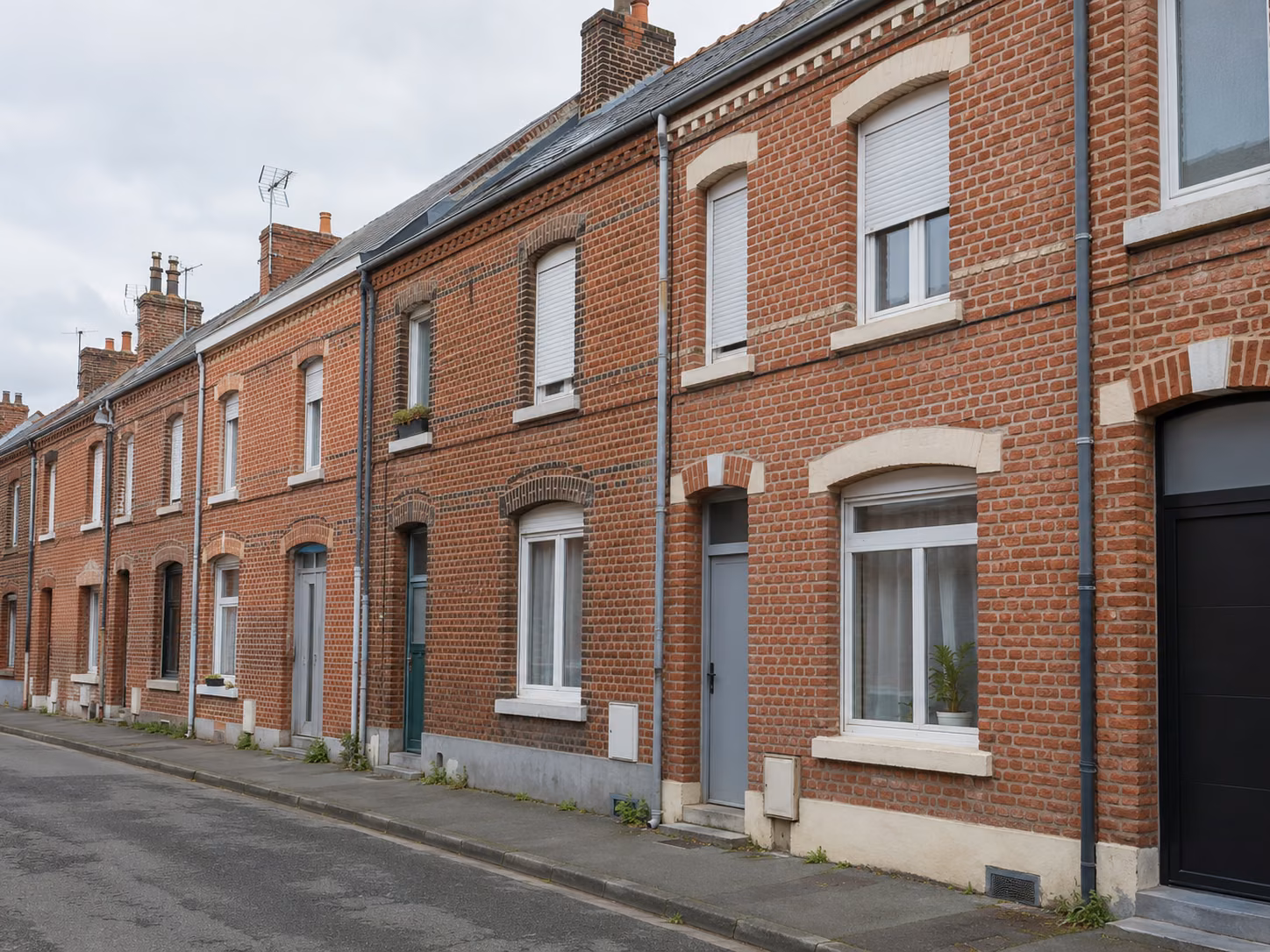Une rue de corons à Lens, façades en brique alignées, portes colorées, trottoir étroit, ciel couvert