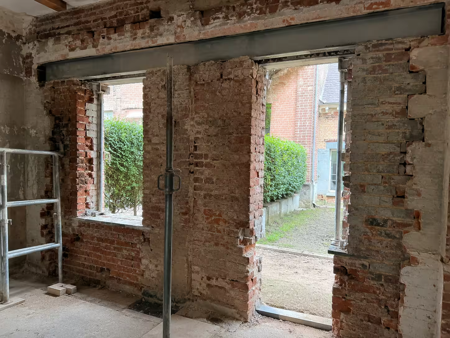 Grandes ouvertures percées dans un mur de brique, échelle appuyée, maison en cours de rénovation