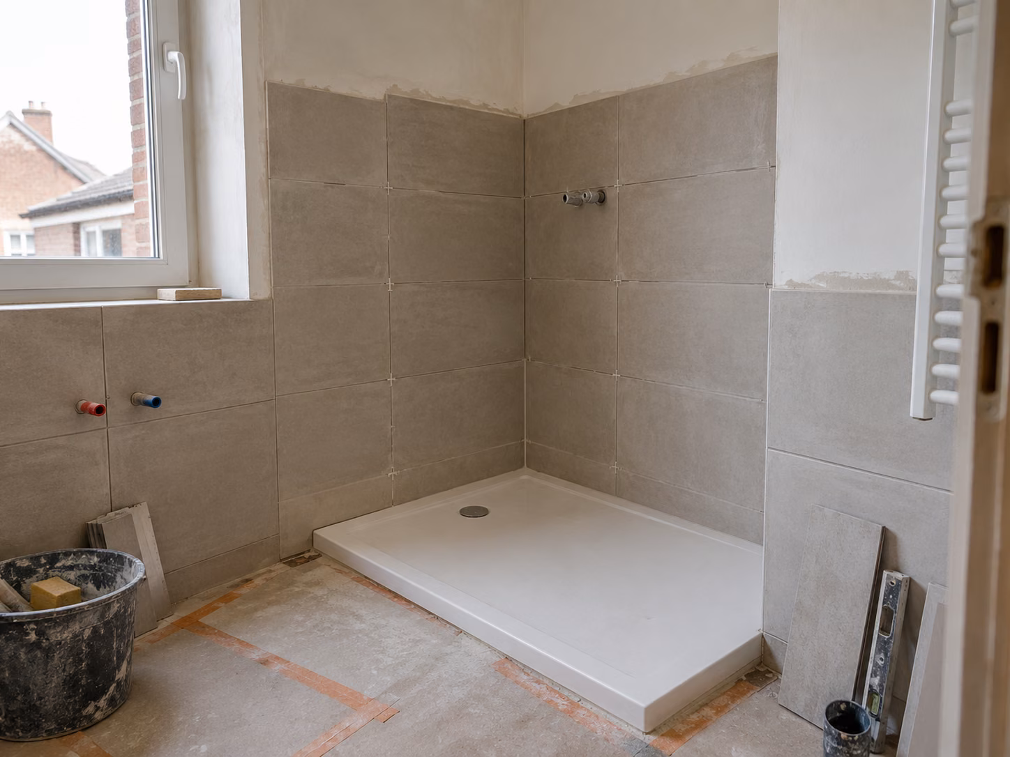 Une salle de bains en cours de finition, receveur de douche extra-plat posé, faïence claire jusqu’à mi-hauteur, joints frais