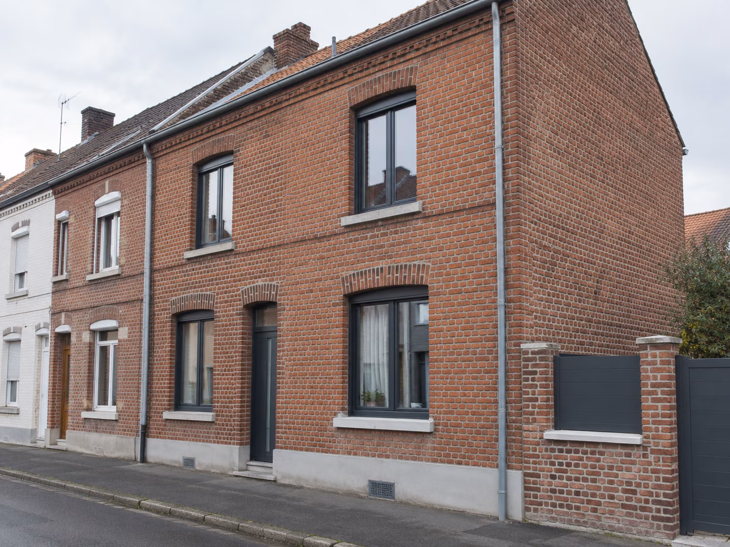 Une façade en brique rénovée avec menuiseries neuves, vue de trois quarts depuis le trottoir