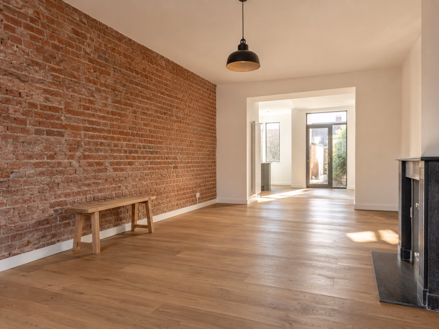 Un séjour de maison en brique entièrement rénové, mur de brique conservé, parquet clair, lumière traversante