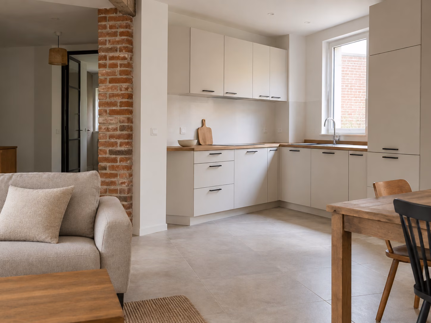 Une cuisine ouverte sur séjour dans une maison ancienne rénovée, plan de travail bois, sol carrelé clair