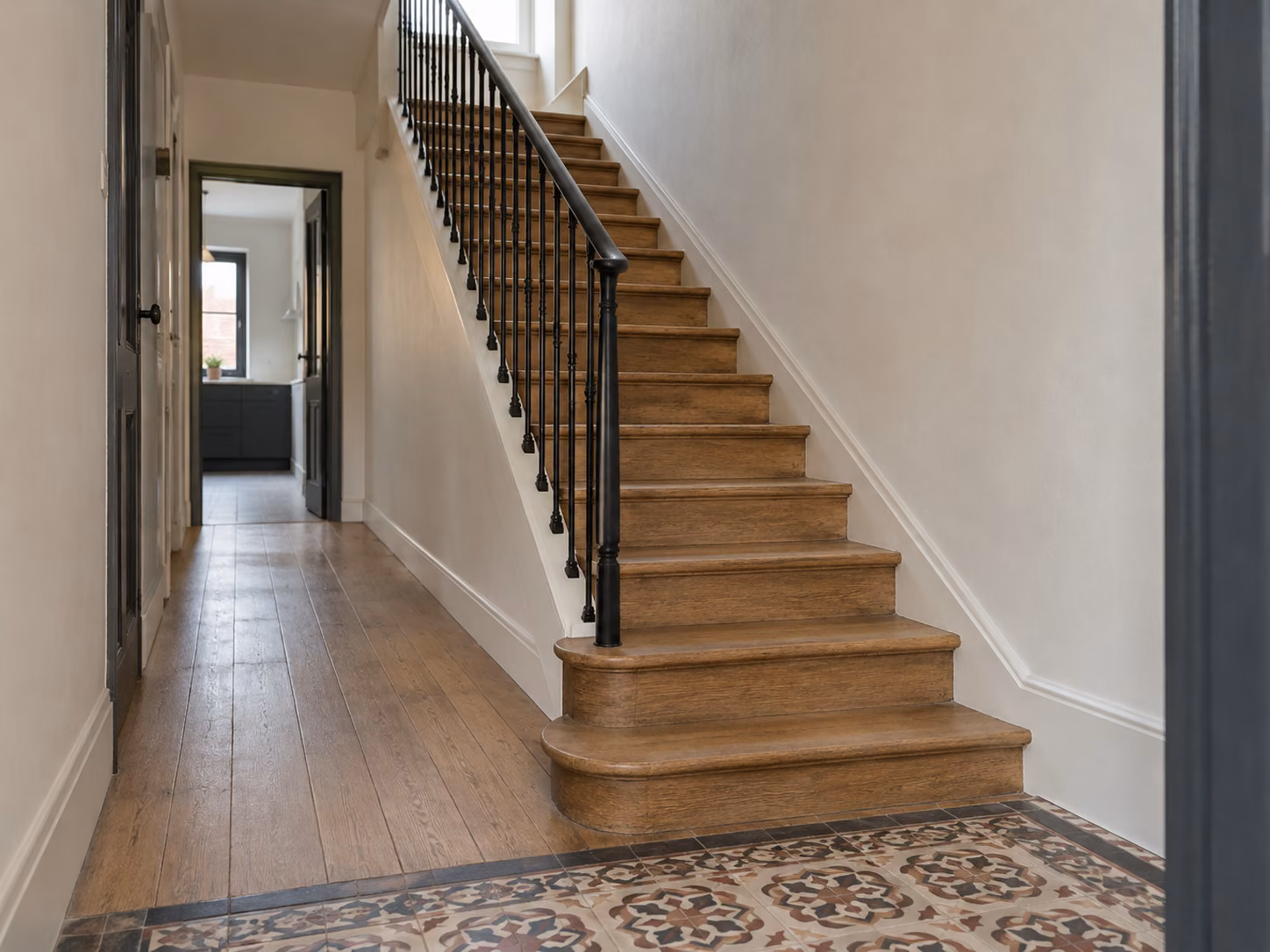Un couloir et un escalier bois refaits dans une maison de ville, mur blanc, rampe métallique noire