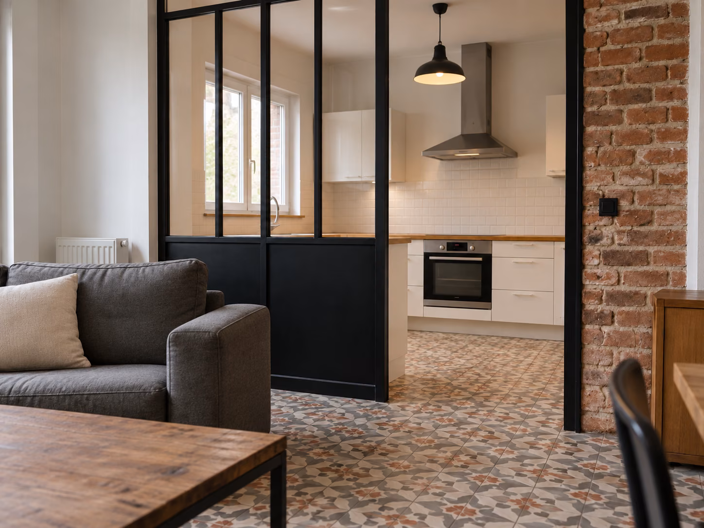Une pièce à vivre rénovée avec verrière d’atelier séparant l’espace cuisine, sol en carreaux de ciment