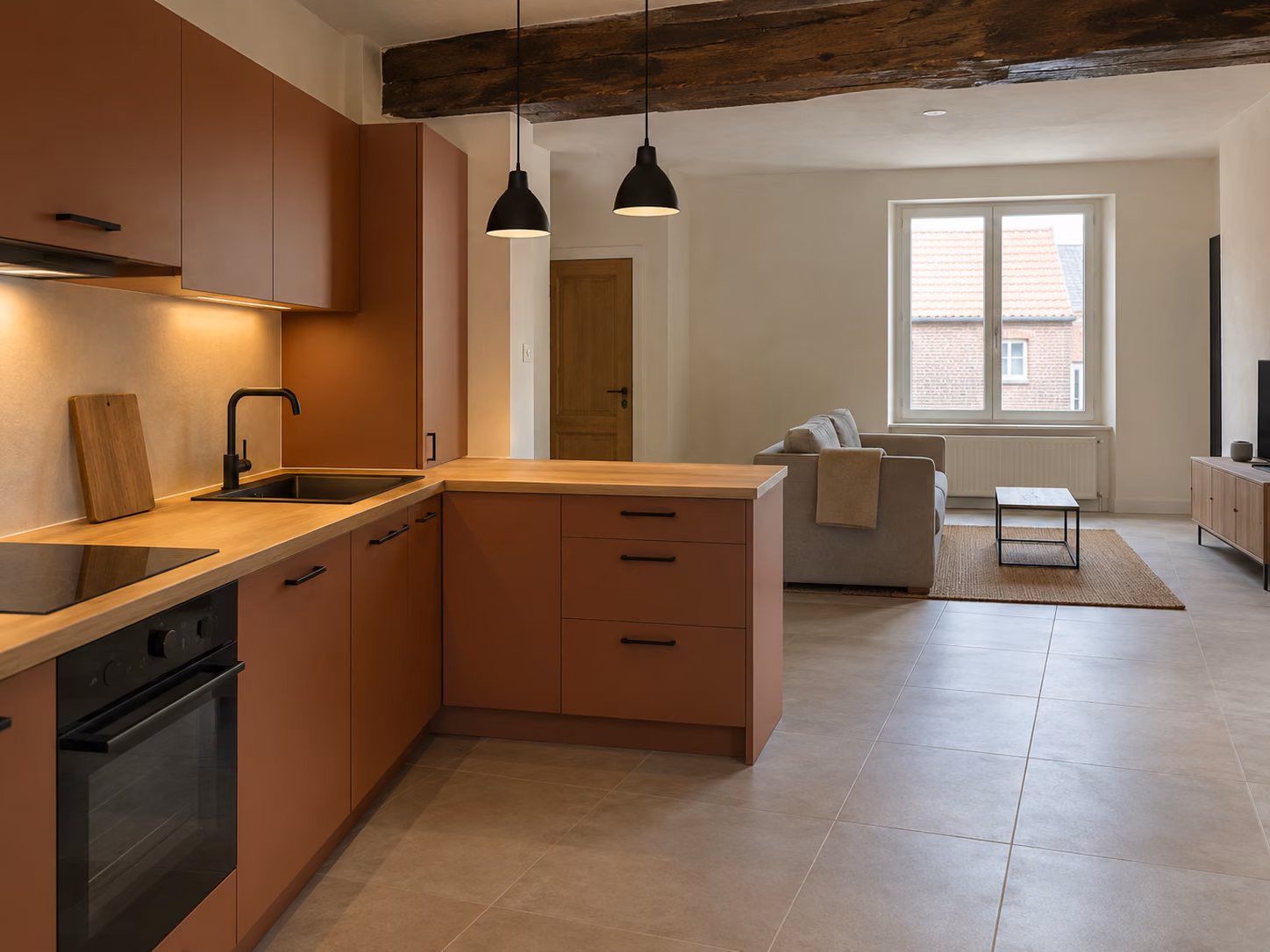 Une cuisine ouverte sur séjour dans une maison ancienne rénovée, plan de travail bois, sol carrelé clair