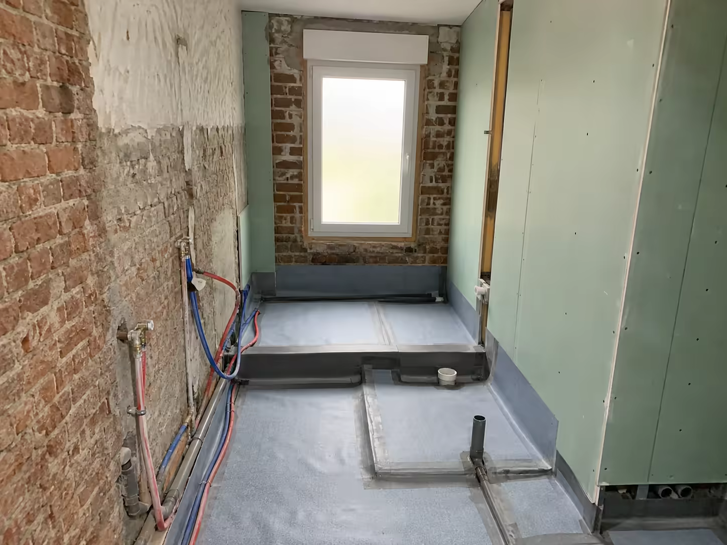 Zone de douche étanchée avec plaques hydrofuges et réseaux encastrés contre un mur de brique ancien