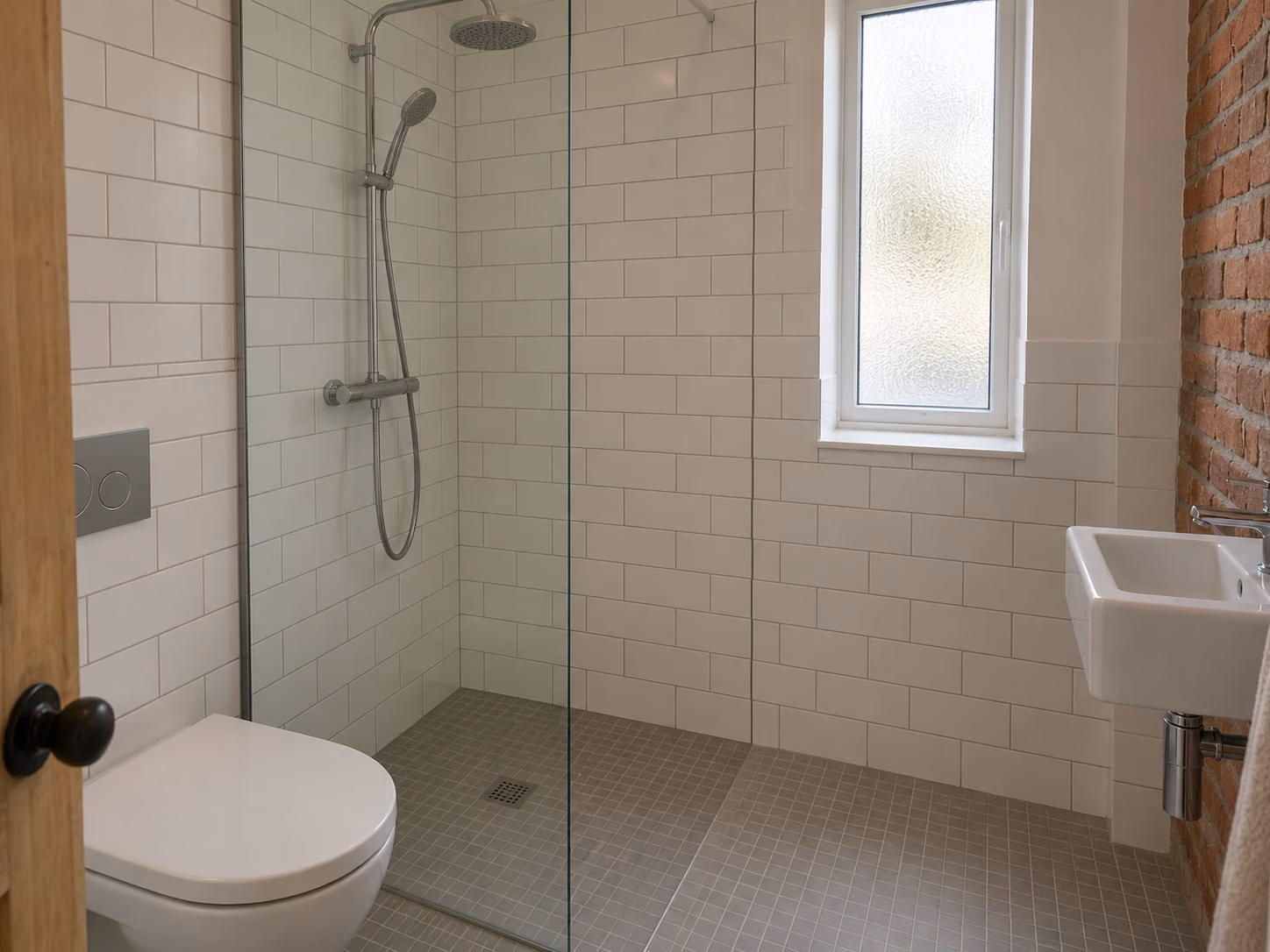 Une salle d’eau compacte avec douche à l’italienne, paroi vitrée, carrelage blanc à joints gris