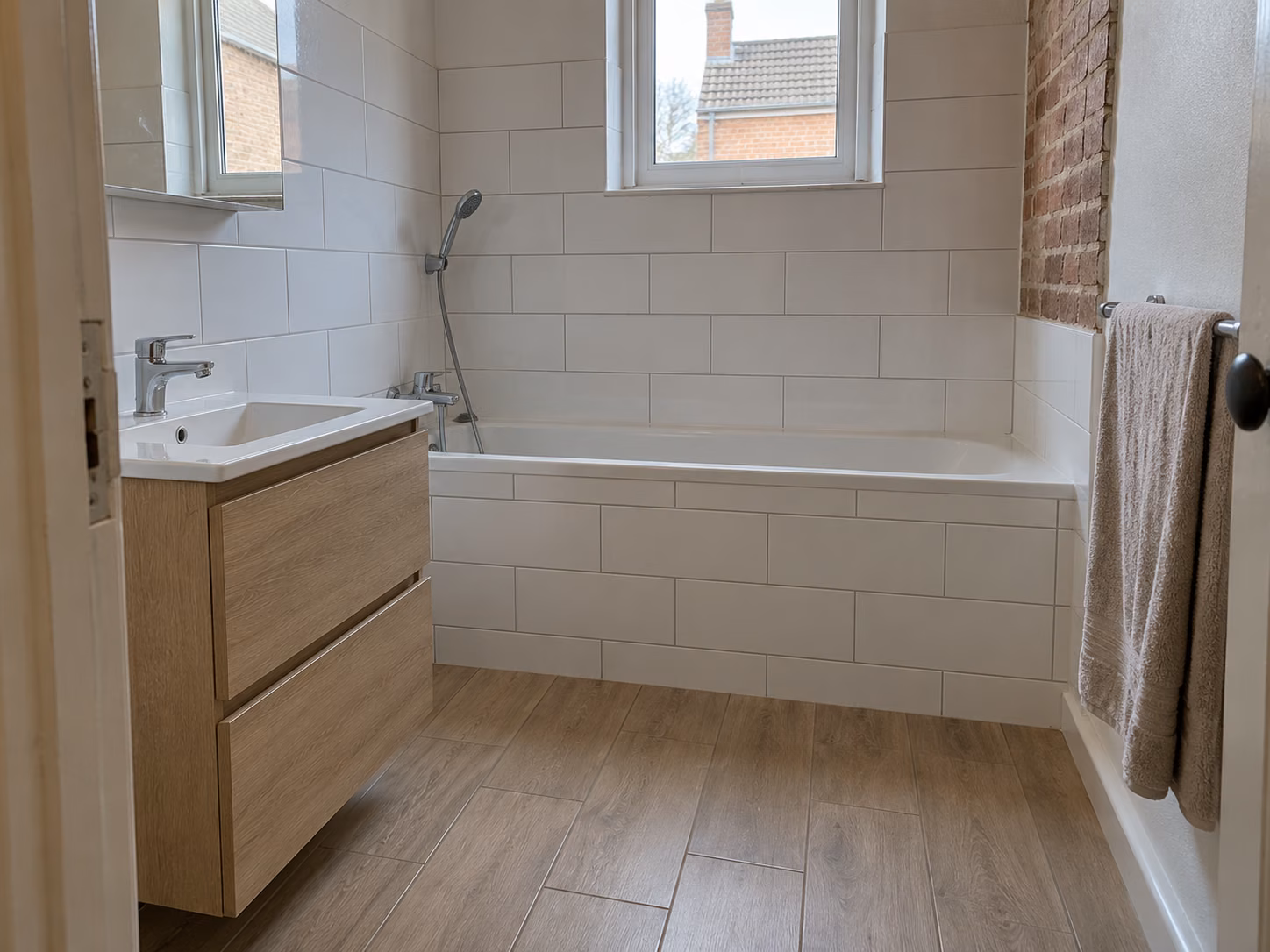 Une salle de bains familiale avec baignoire encastrée, faïence blanche et sol imitation parquet