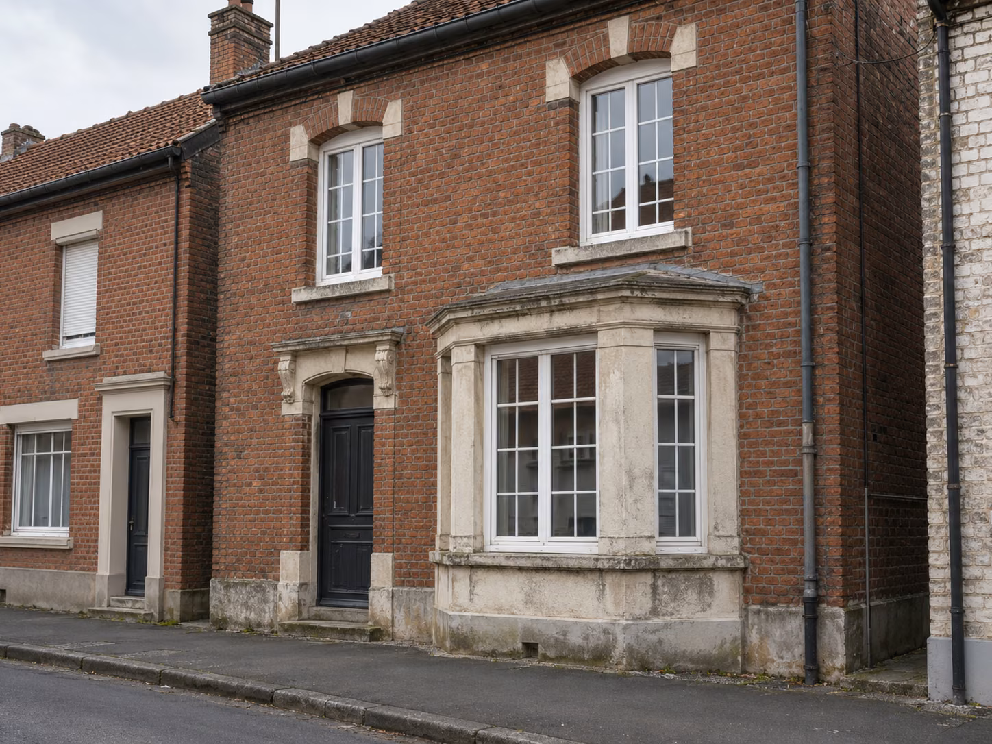 Une façade de maison 1930 en brique avec bow-window, encadrements en pierre et menuiseries à petits bois