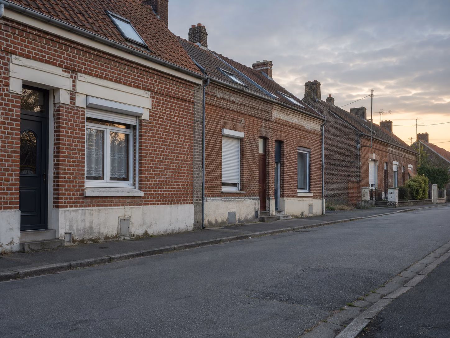 Une rue résidentielle calme, maisons en brique des années 1930, voitures absentes, éclairage de fin de journée