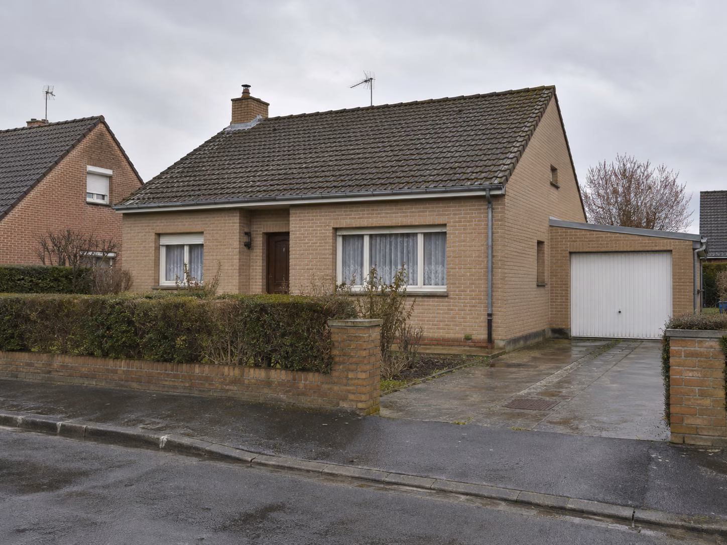 Un pavillon des années 1960 en brique claire avec garage attenant, haie taillée, allée en pavés