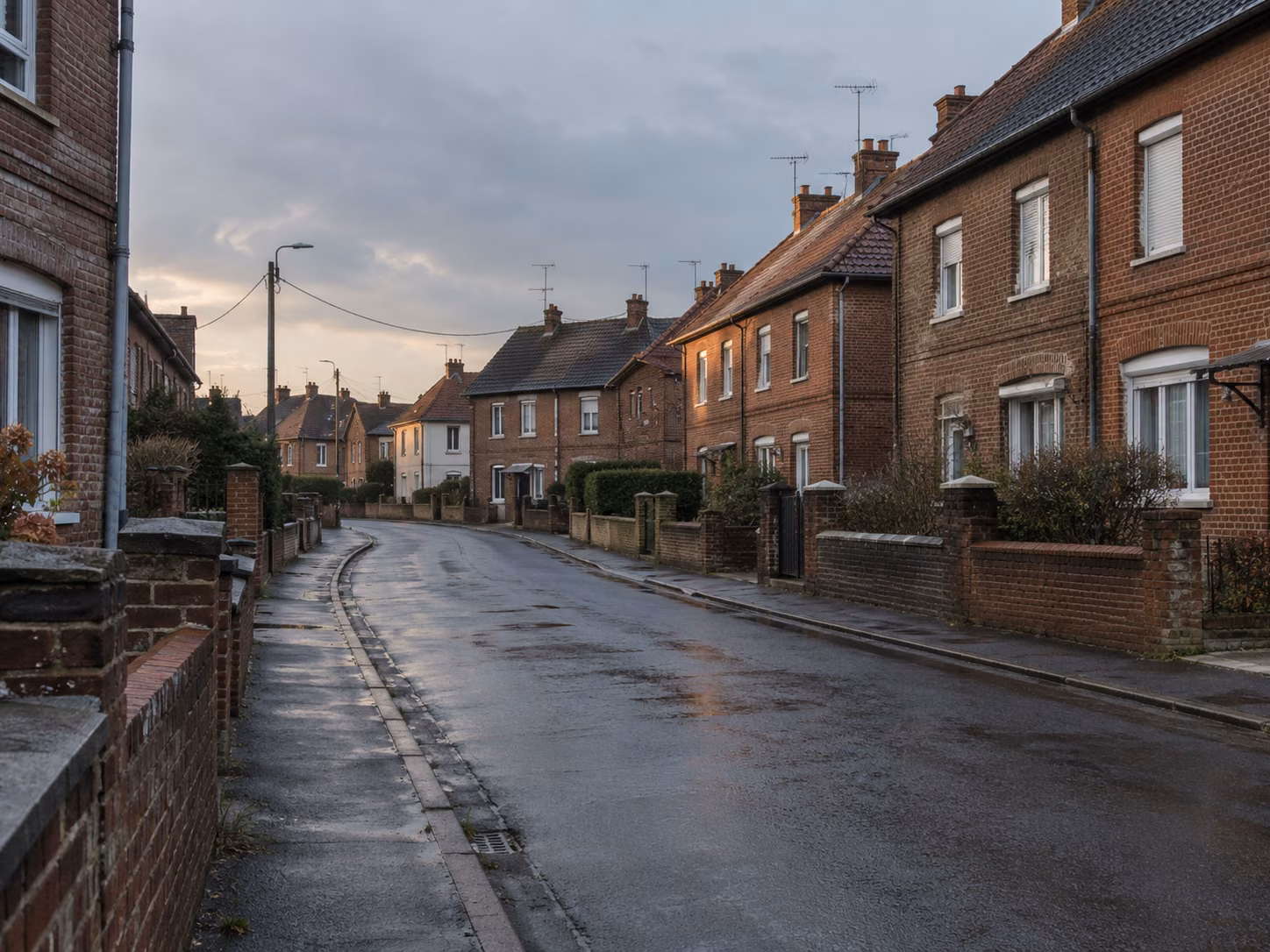 Une rue résidentielle calme, maisons en brique des années 1930, voitures absentes, éclairage de fin de journée
