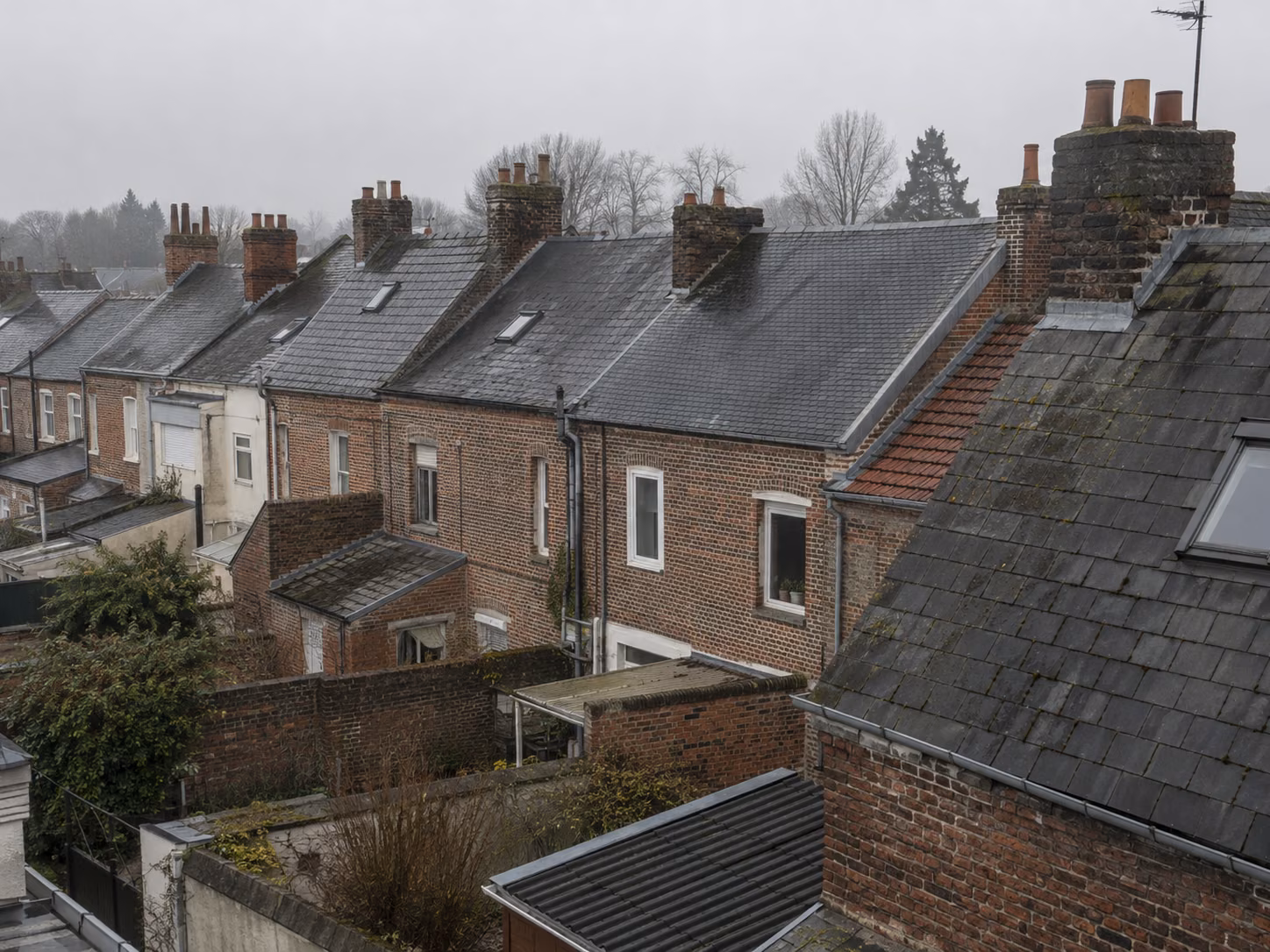 Une rangée de maisons en bande avec toitures en ardoise et souches de cheminée alignées, vue en légère plongée