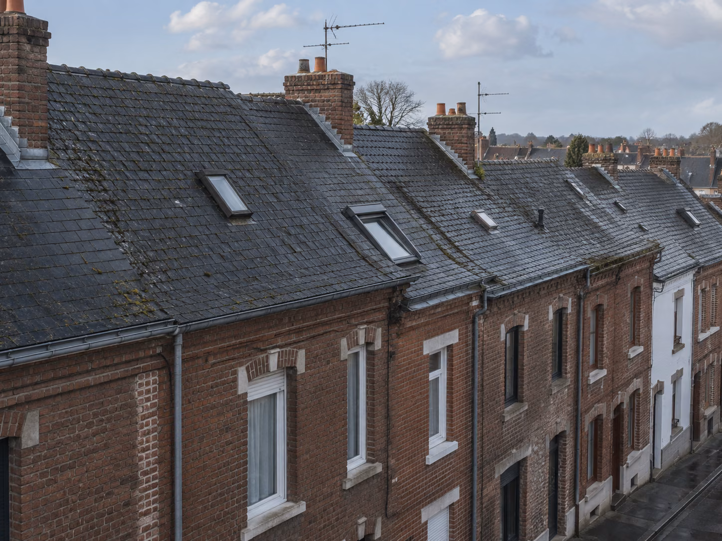 Une rangée de maisons en bande avec toitures en ardoise et souches de cheminée alignées, vue en légère plongée